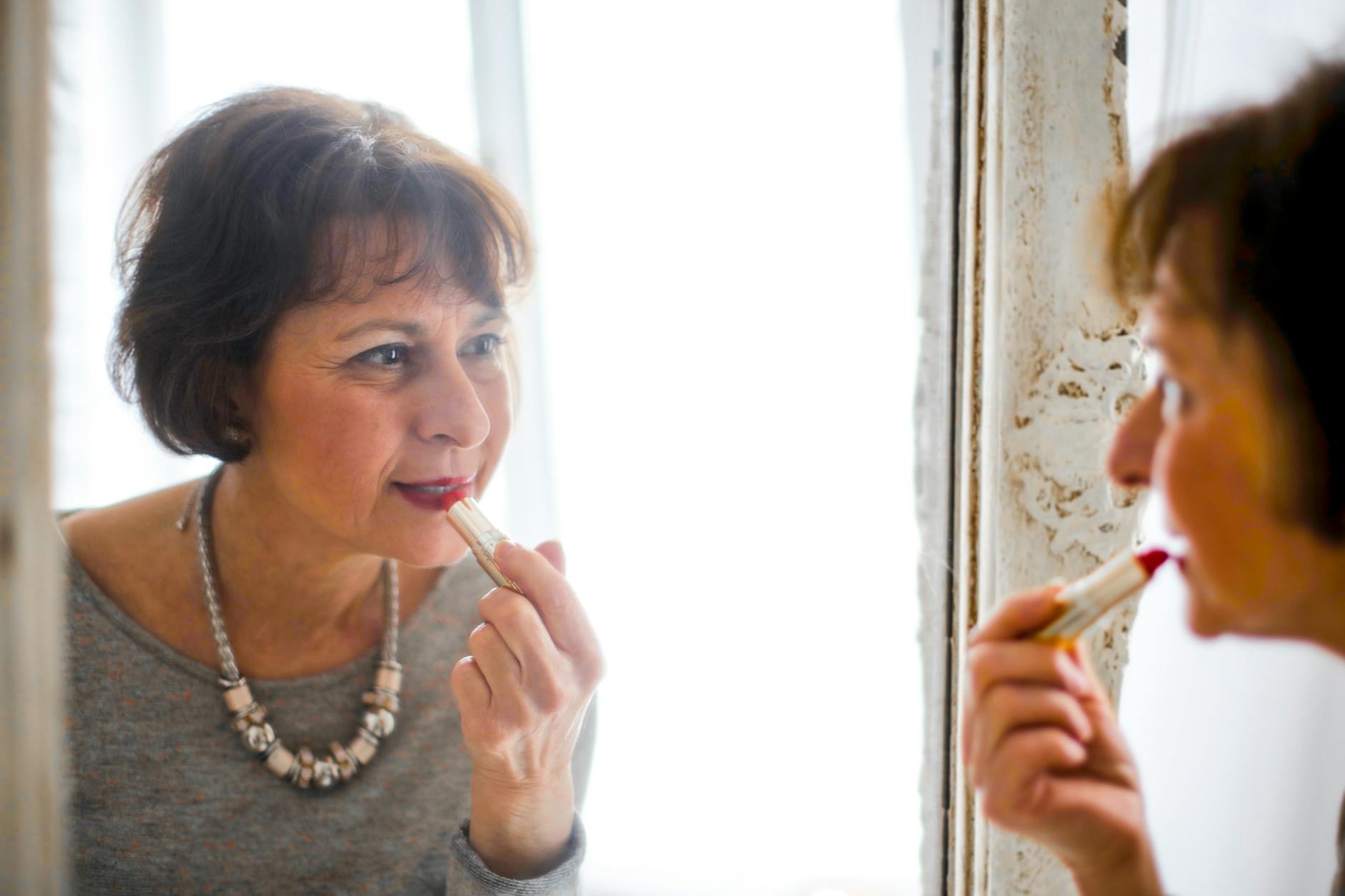 photo of older woman applying lipstick in front of the mirror